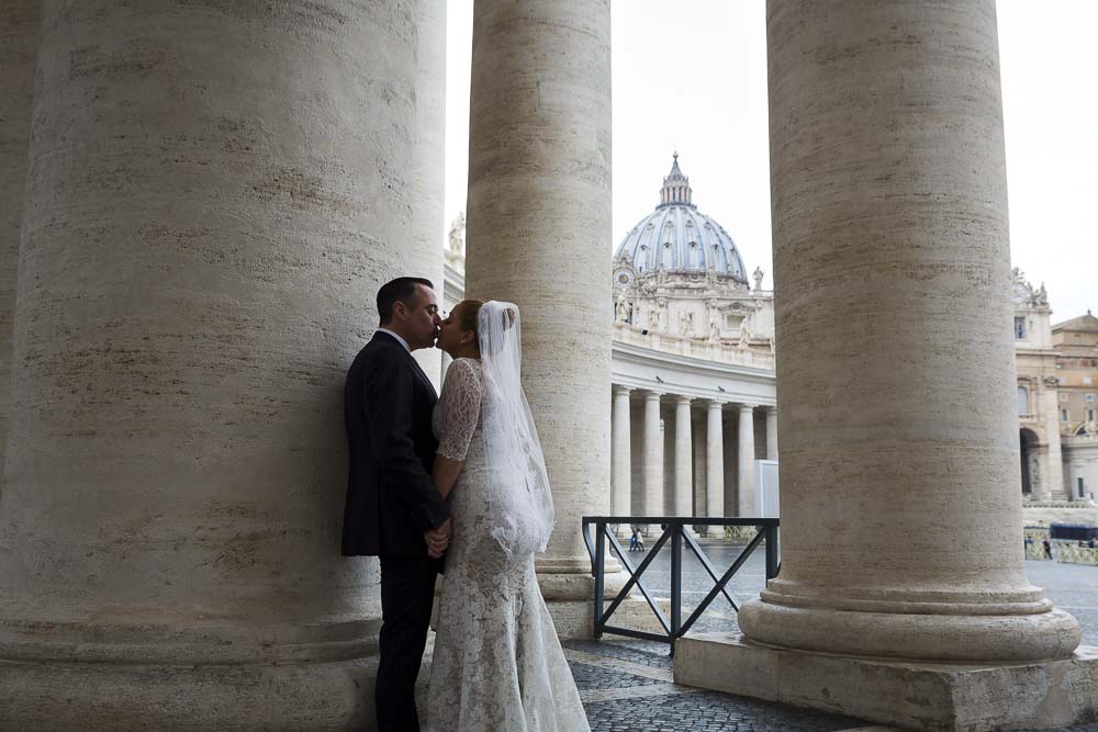 Kissing in Saint Peter's square with the Basilica dome in the far distance. Wedding Blessing Photography in Rome, Italy.