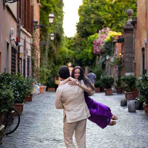 Twirling around cinematic style photos of a couple having fun during their engagement photoshoot on a typical roman ancient alleyway street