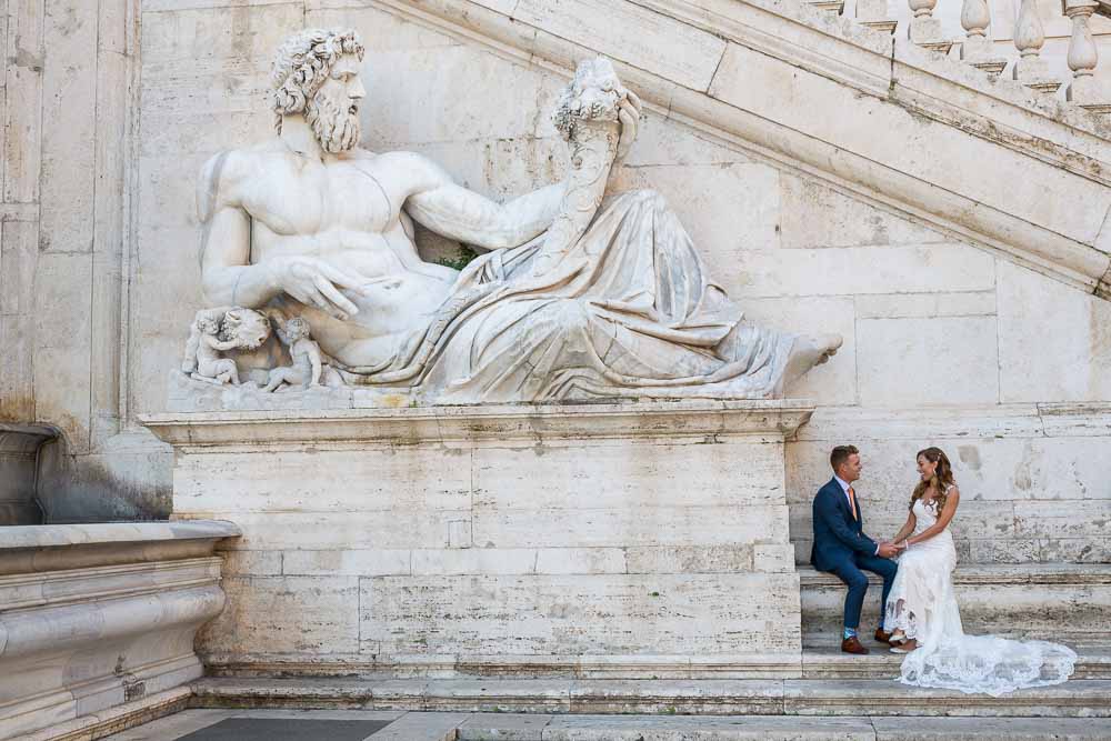 Bride & groom sitting next to a large roman marble statue