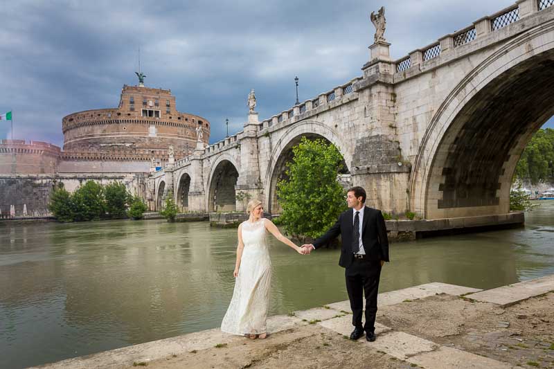 Holding hands down below the Tiber river with the Castle far distance