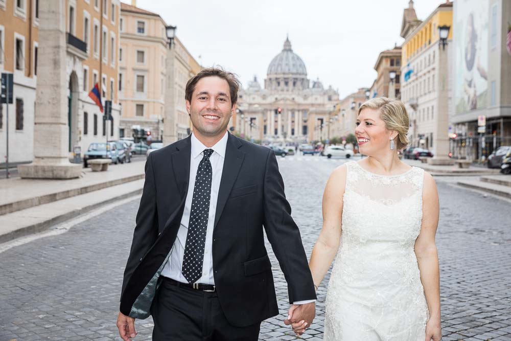 Bride and groom Novelli Sposi holdings hands and walking together in Via della Conciliazione with Saint Peter's background while on a honeymoon photography session 