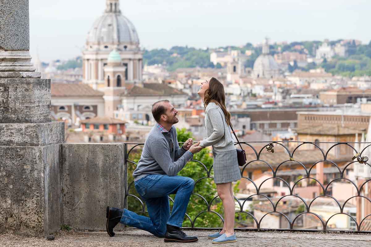 Man kneeling down during a surprise wedding proposal taking place at the scenic parco del pincio terrace Italy