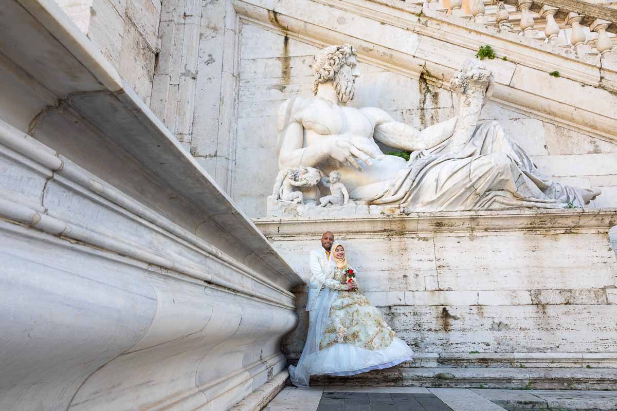 Taking newlywed pictures together under ancient roman statue in white marble