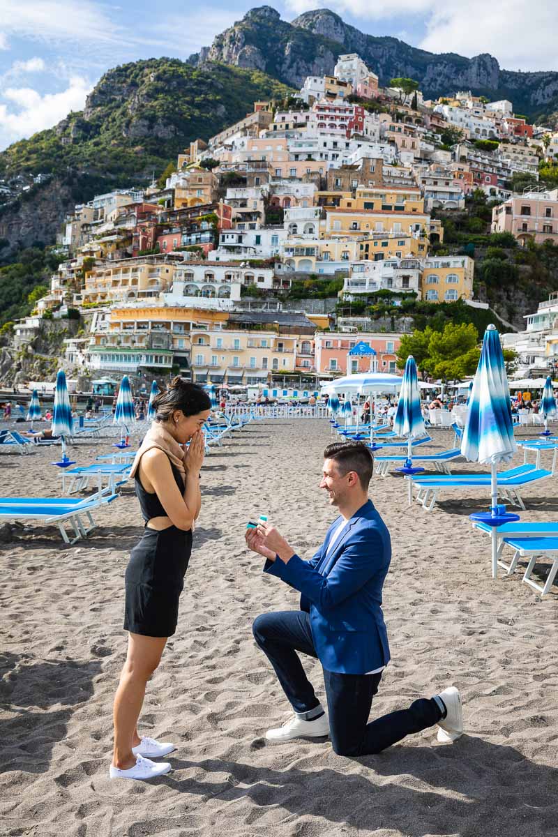 Telephoto composition of a surprise marriage proposal on the Positano beach overlooking the vertical town in the background 