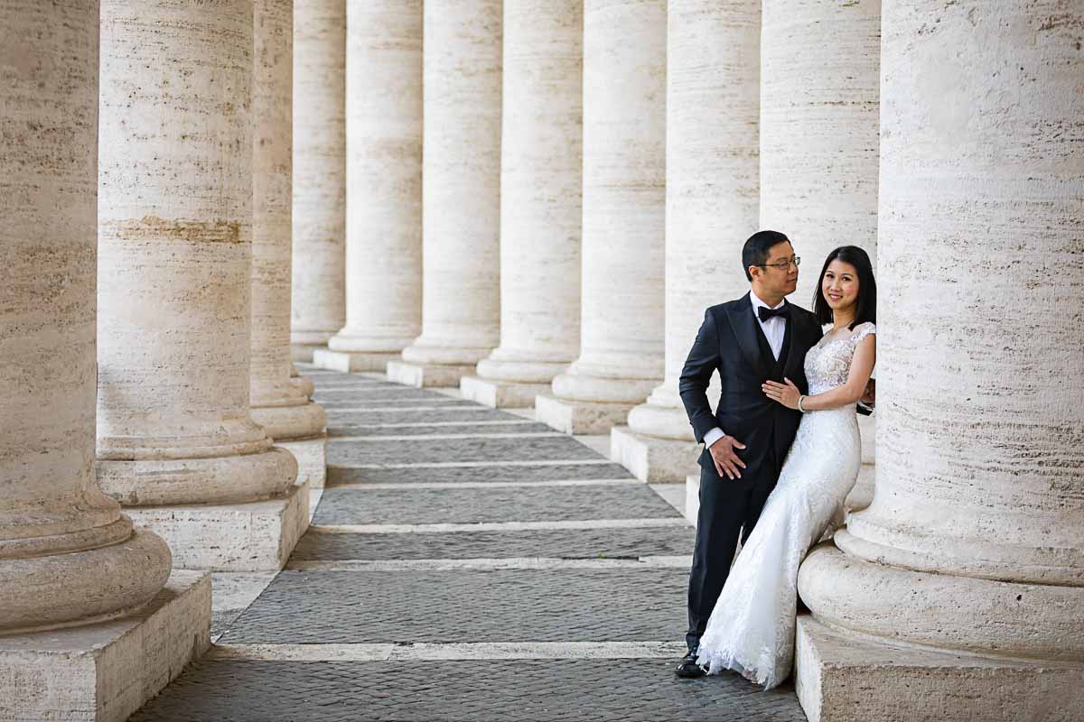Couple posing underneath the Vatican's colonnade dressed in matrimonial attire
