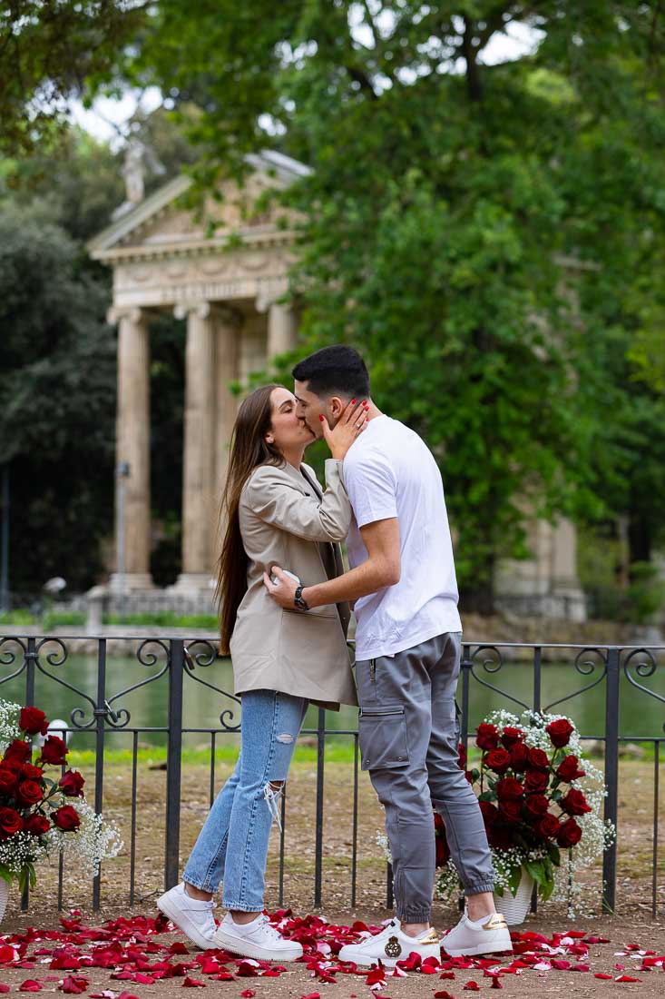 Engaged by the Borghese park among a bouquet of red roses and a scenic view over the lake and the temple
