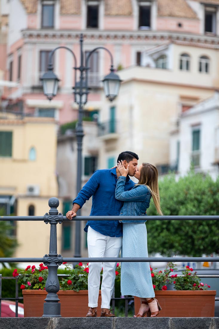 Kissing town while standing behind a railing with buildings in the backdrop of the photo shoot