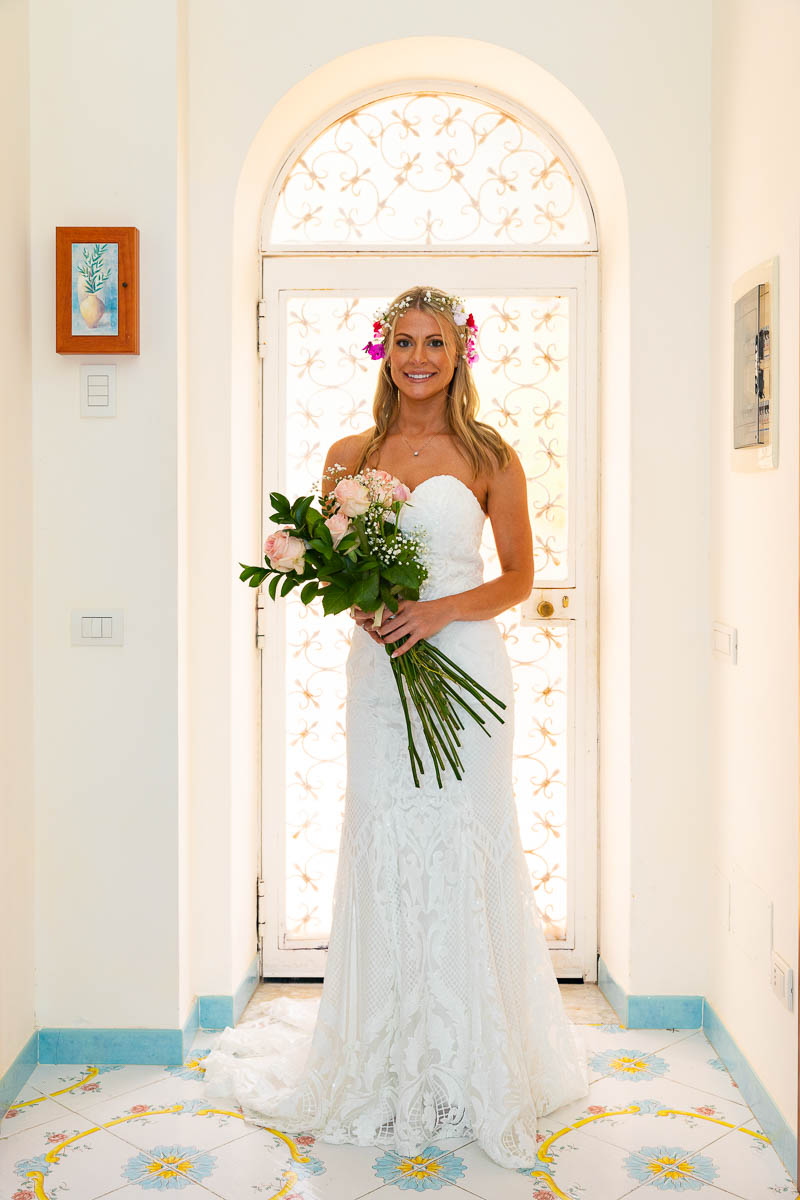 Full view of bride and wedding gown standing indoor by the entrance 