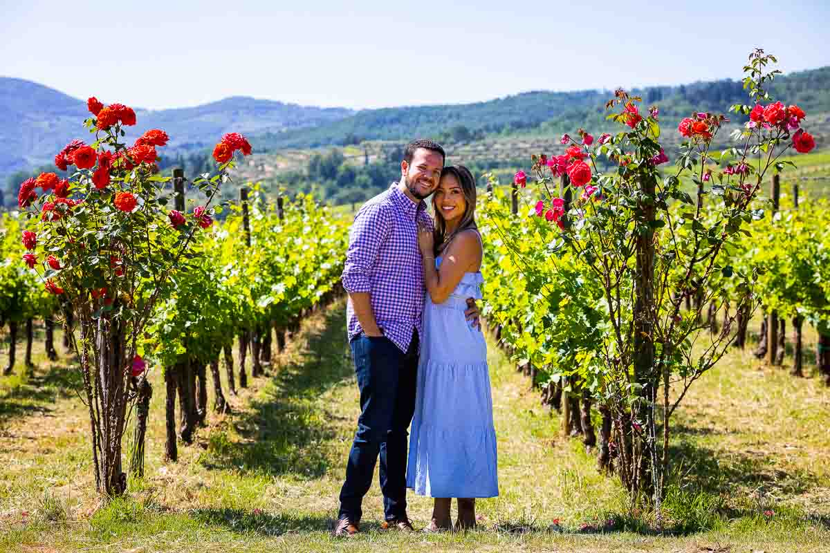Portrait of a couple together posing in front row vineyard where beautiful red roses were placed. Posing after a Vineyard engagement 