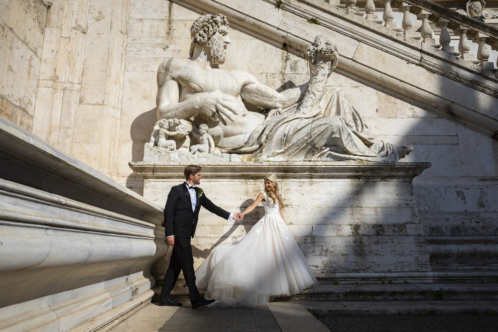 Newlywed couple walking together under a white marble statue