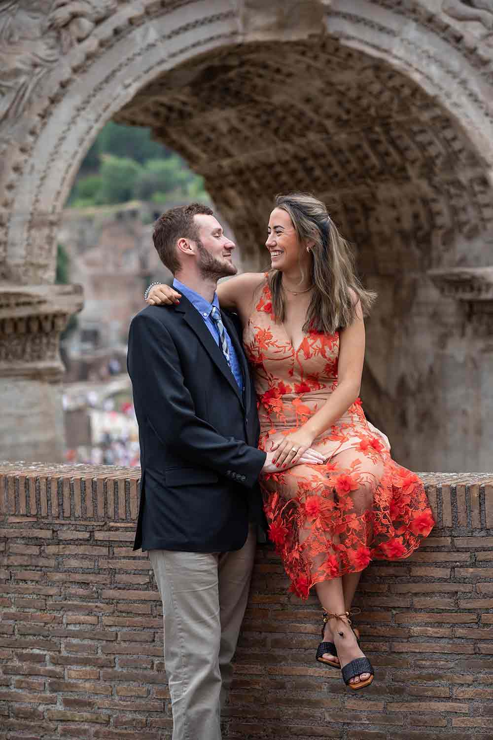 Couple portrait taken underneath the Arch of Septimius Severus while sitting down on a small brick wall