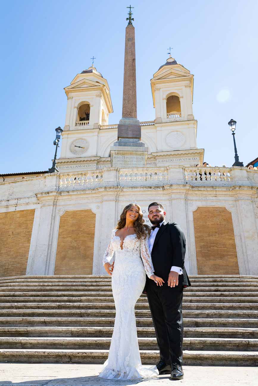 Newlyweds posing for a wedding photo on the Spanish steps with Church Trinità dei Monti background