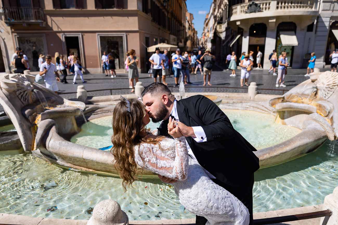 Groom kissing the bride in front barcaccia water fountain found bottom Spanish steps background people out of focus