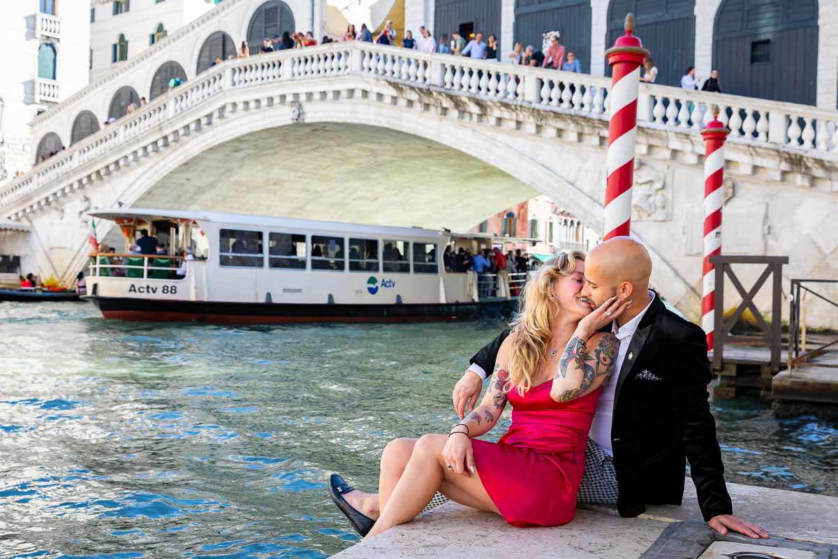 Couple sitting down next to the grand canal with the bridge backdrop