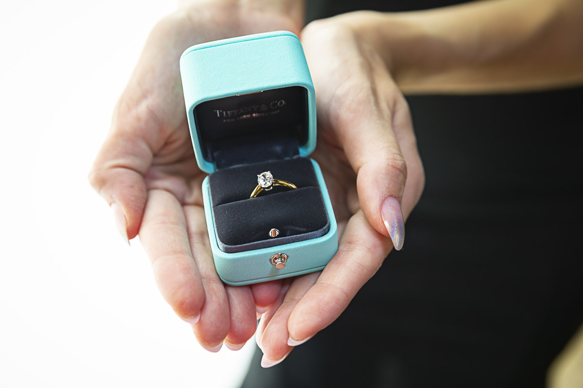 Showing with two hands the engagement ring still contained in the ring box