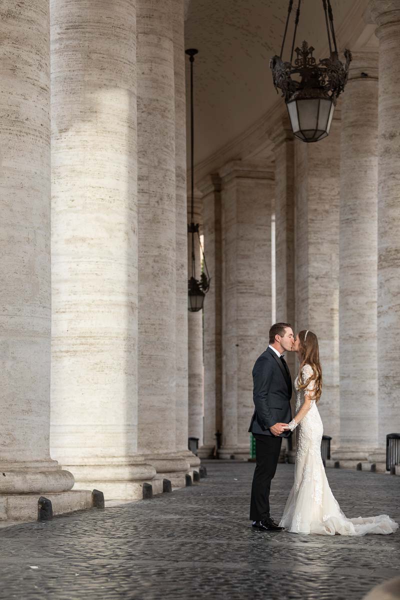 Bride and groom kissing underneath the majestic columns surrounding Saint Peter's square Vatican