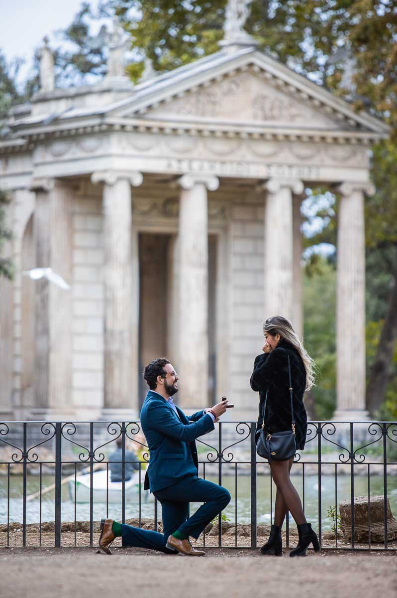 Knee down wedding marriage proposal candidly photographed from a distance Borghese park in front of Asclepius Temple