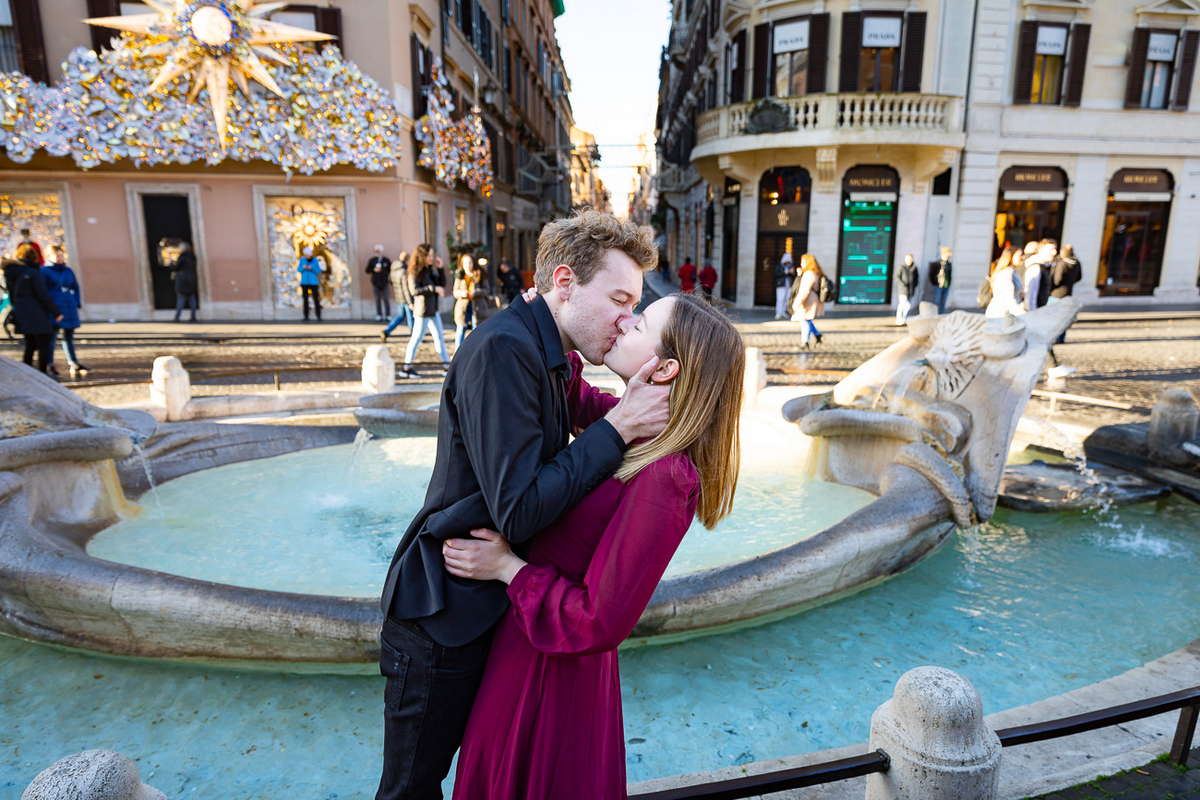 Couple passionately kissing next to the Barcaccia water fountain found at the Spanish steps in Rome Italy.