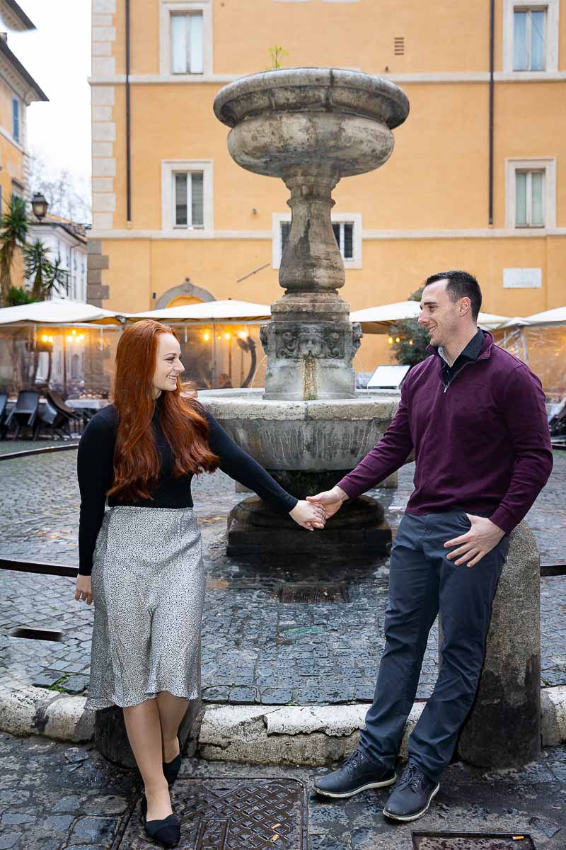 Couple holding hands in a roman Piazza in front of water fountain