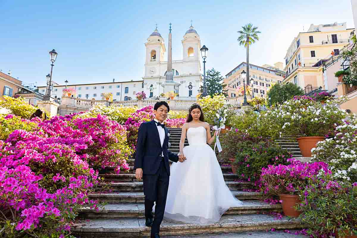 The bride with groom walking down the Spanish staircase in spring while the staircase full of beautiful blooming flowers