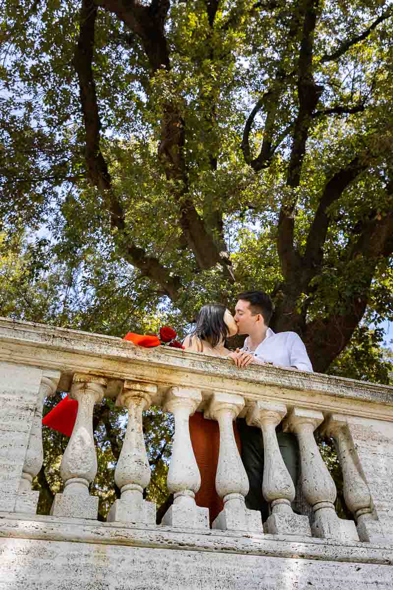 Kissing underneath a green lush tree in the pincio park terrace 