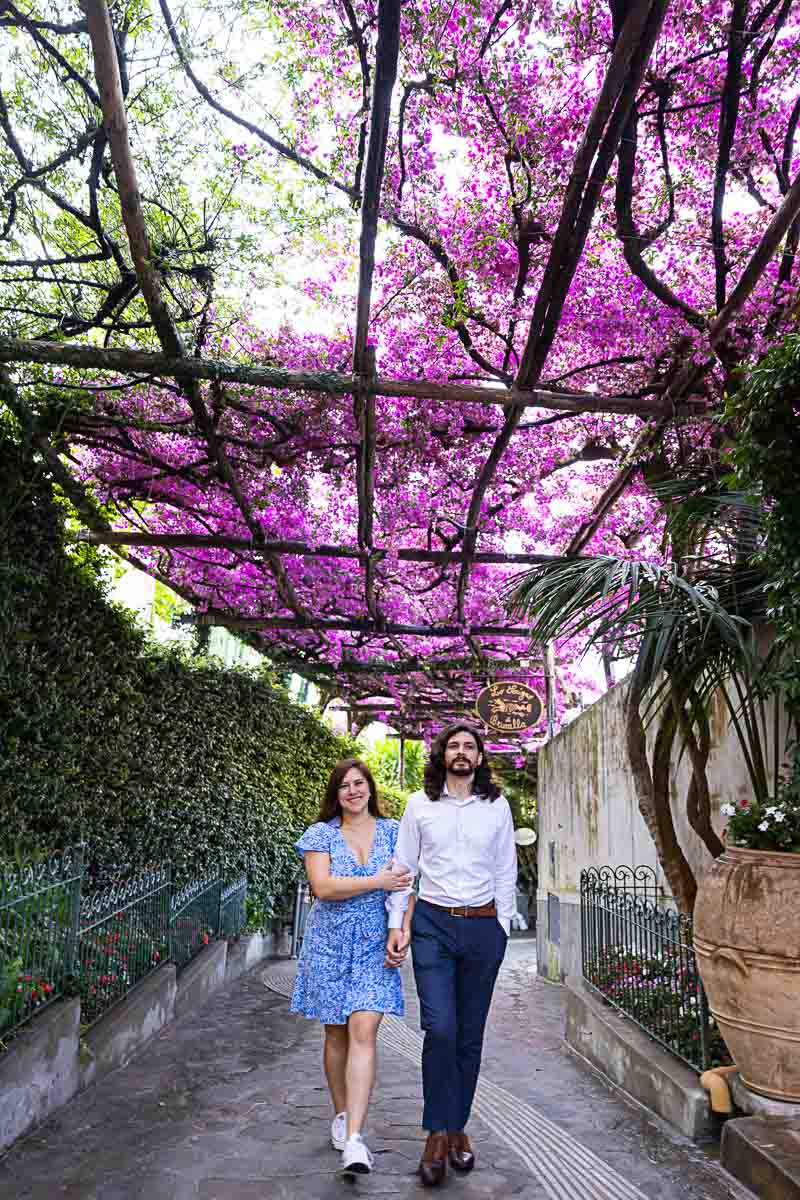 Couple walking under bougainvillea flowers bright fuchsia color over typical alleyway streets
