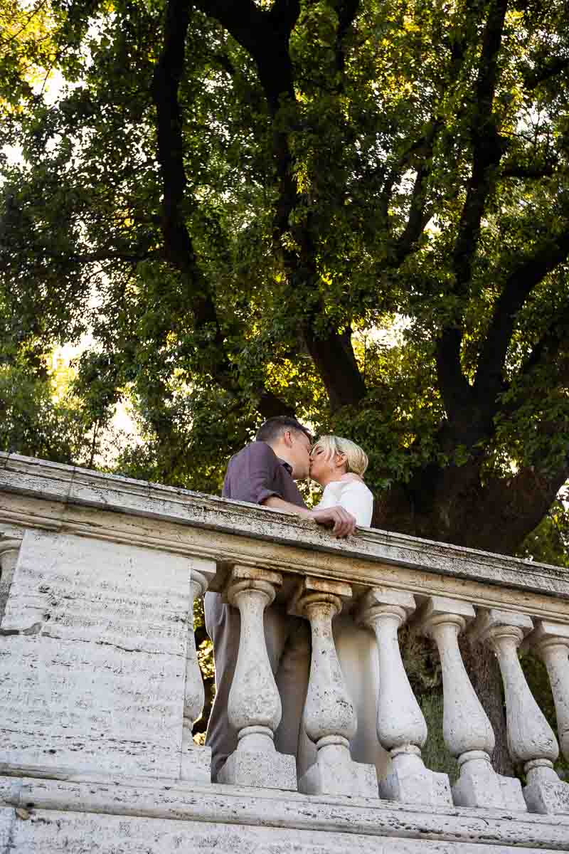Couple portrait photographed in a park under nice green trees behind a marble balconade