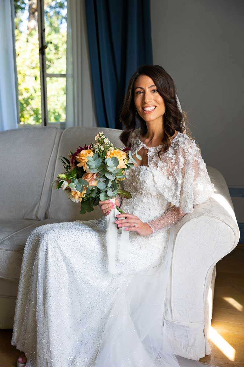 Bride smiling while sitting down and taking bridal pictures by the window