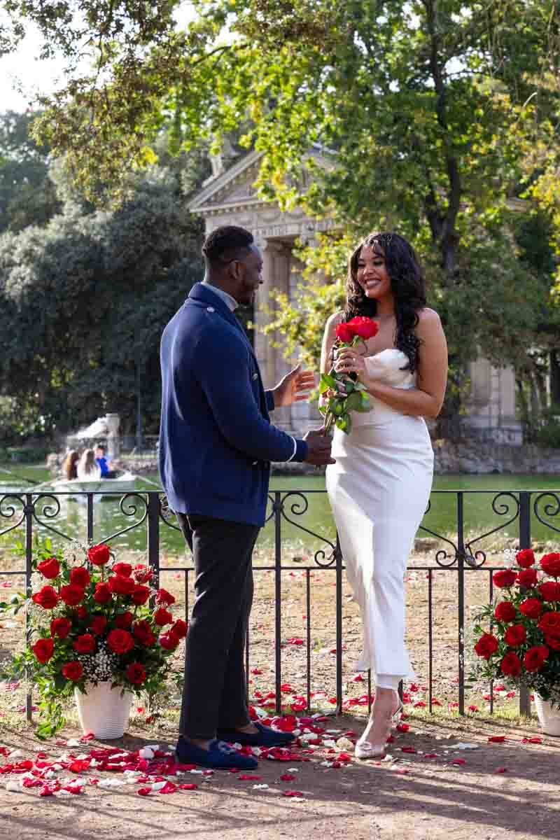 Offering red roses during a photoshoot around the park lake with an ancient temple background 