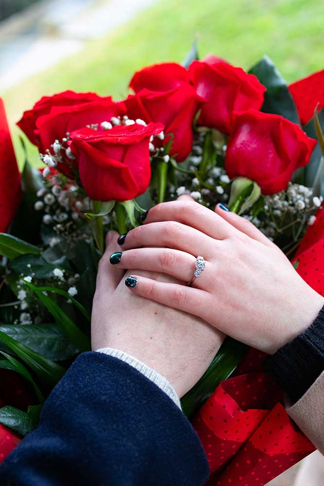 Engagement ring photographed over red roses which holding hands