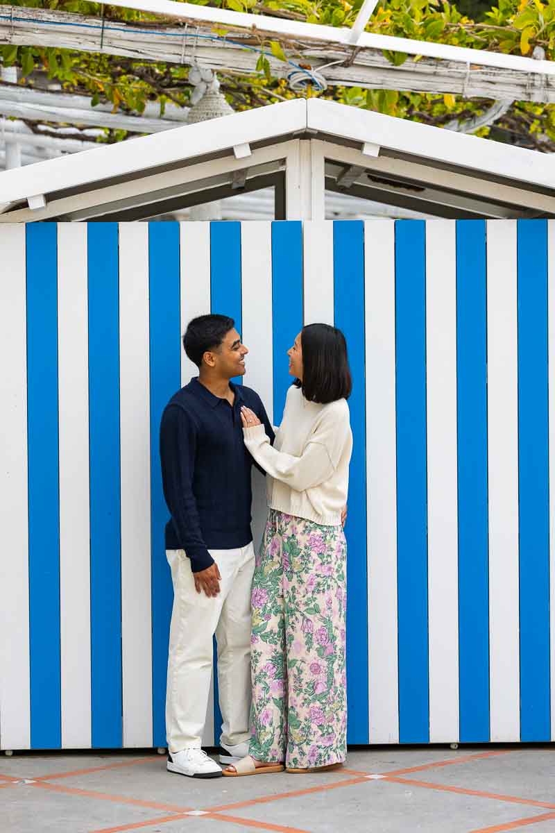 Couple posing in front of beach cabin with blue and white stripes typical summer season 