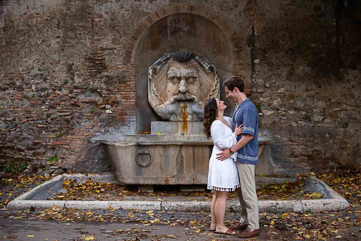 Full figure picture frame of a couple posing in front ancient roman water fountain found in front park entrance