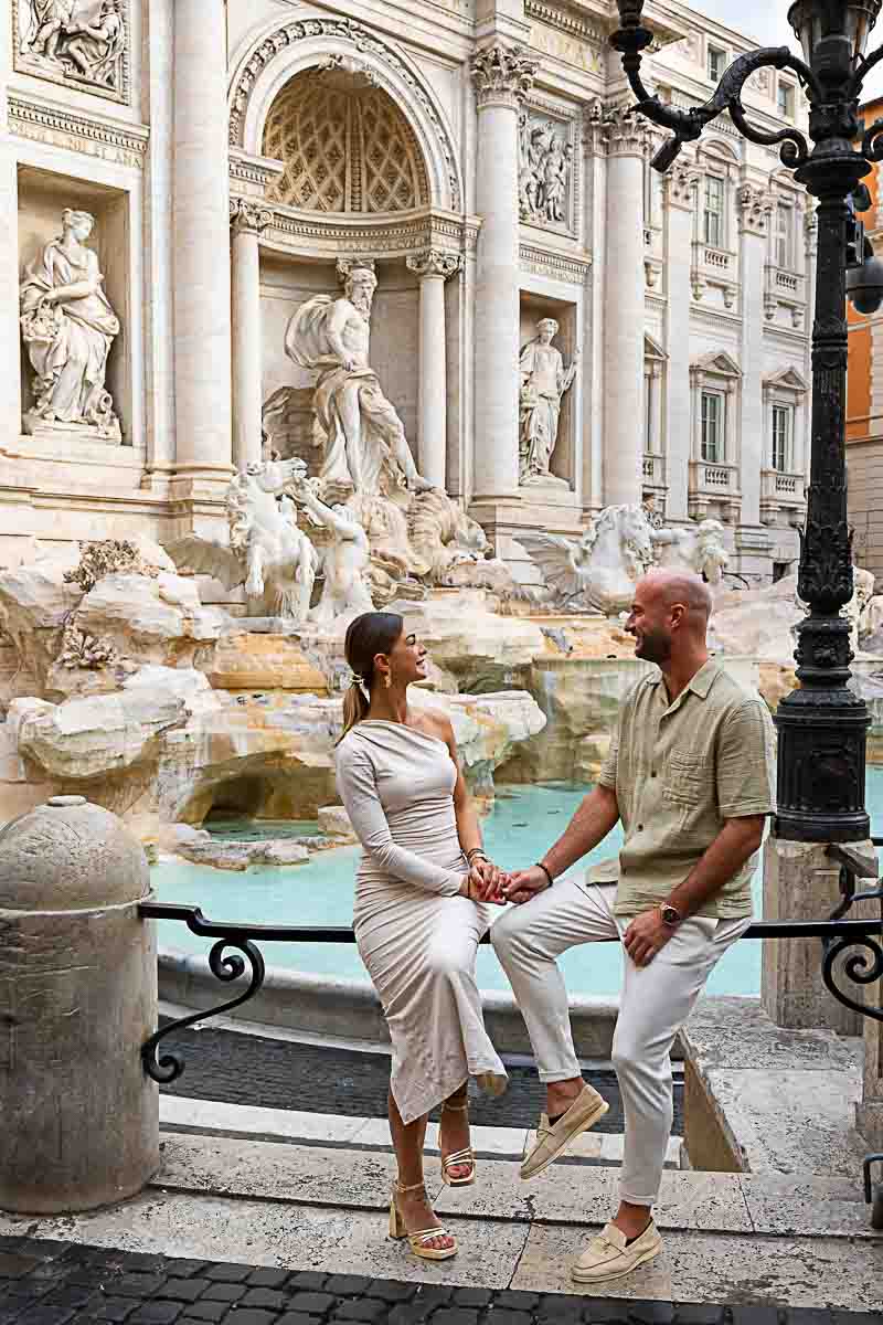 Couple sitting down Trevi fountain during a morning photoshoot taking San Valentine engagement photos