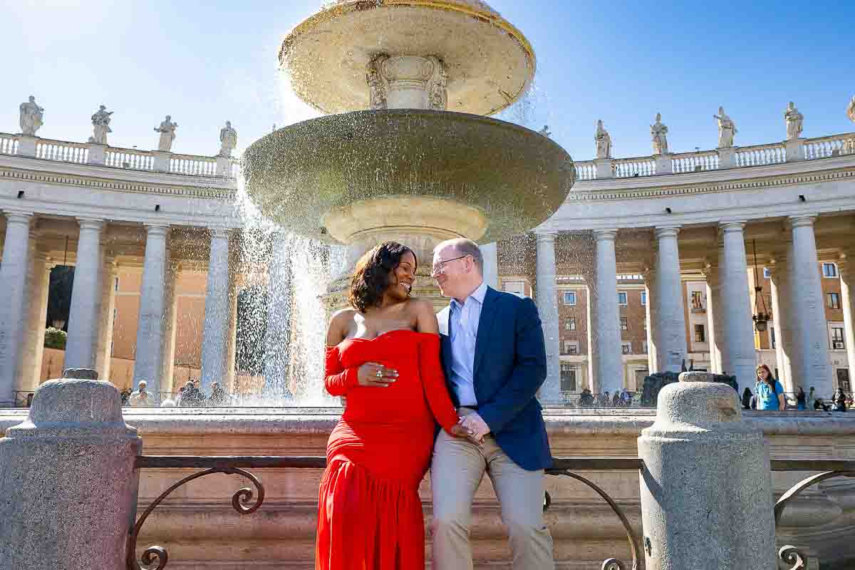 Couple photographed during a maternity photoshoot in Rome sitting on the edge of a water fountain in Saint Peter's square