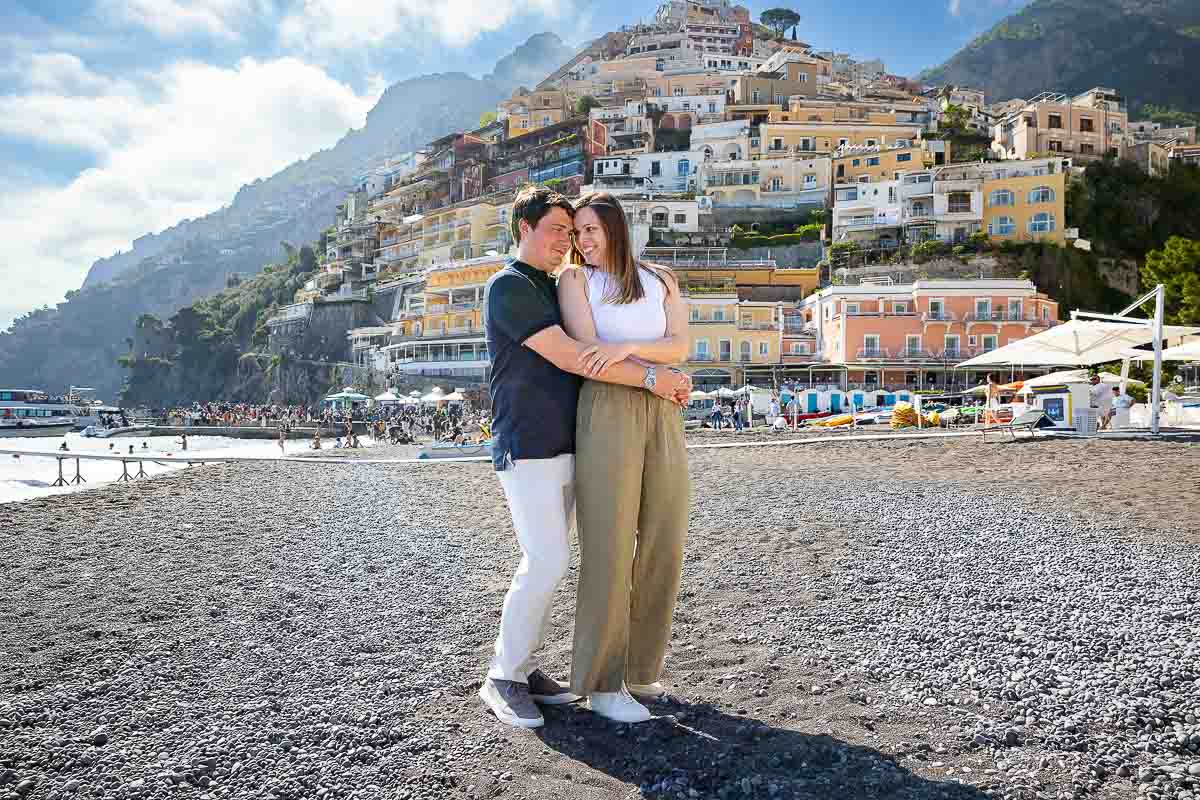Couple posed close together holding each other while taking engagement photos on the beach 