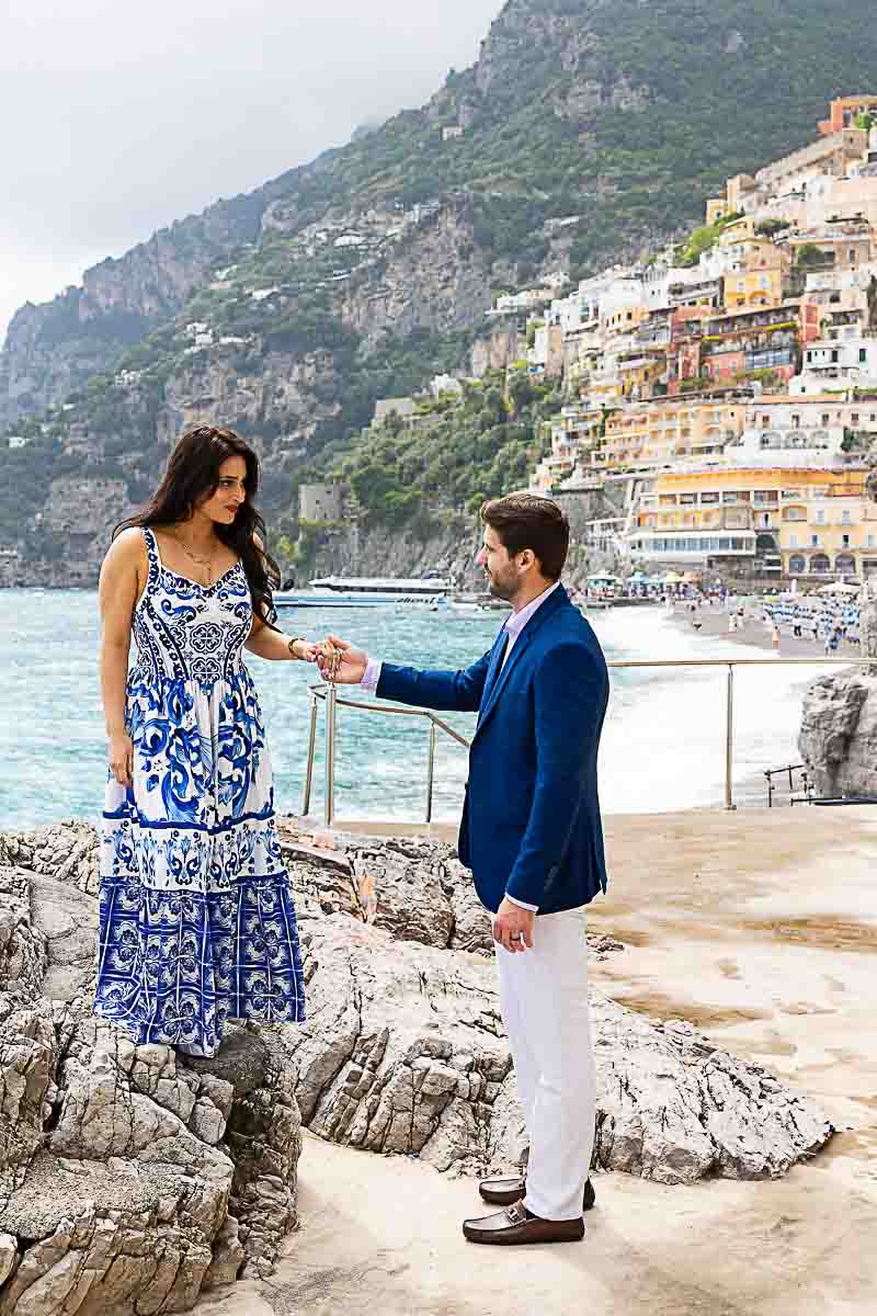 Positano Couples Photoshoot picture taking on the beach on the rocks while looking at the vertical town in the far distance