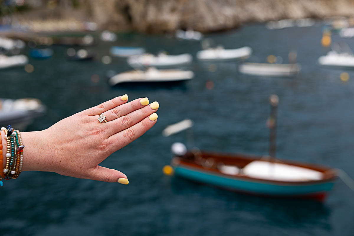 Close up of the engagement ring on hand with the boats out of focus framed in the picture