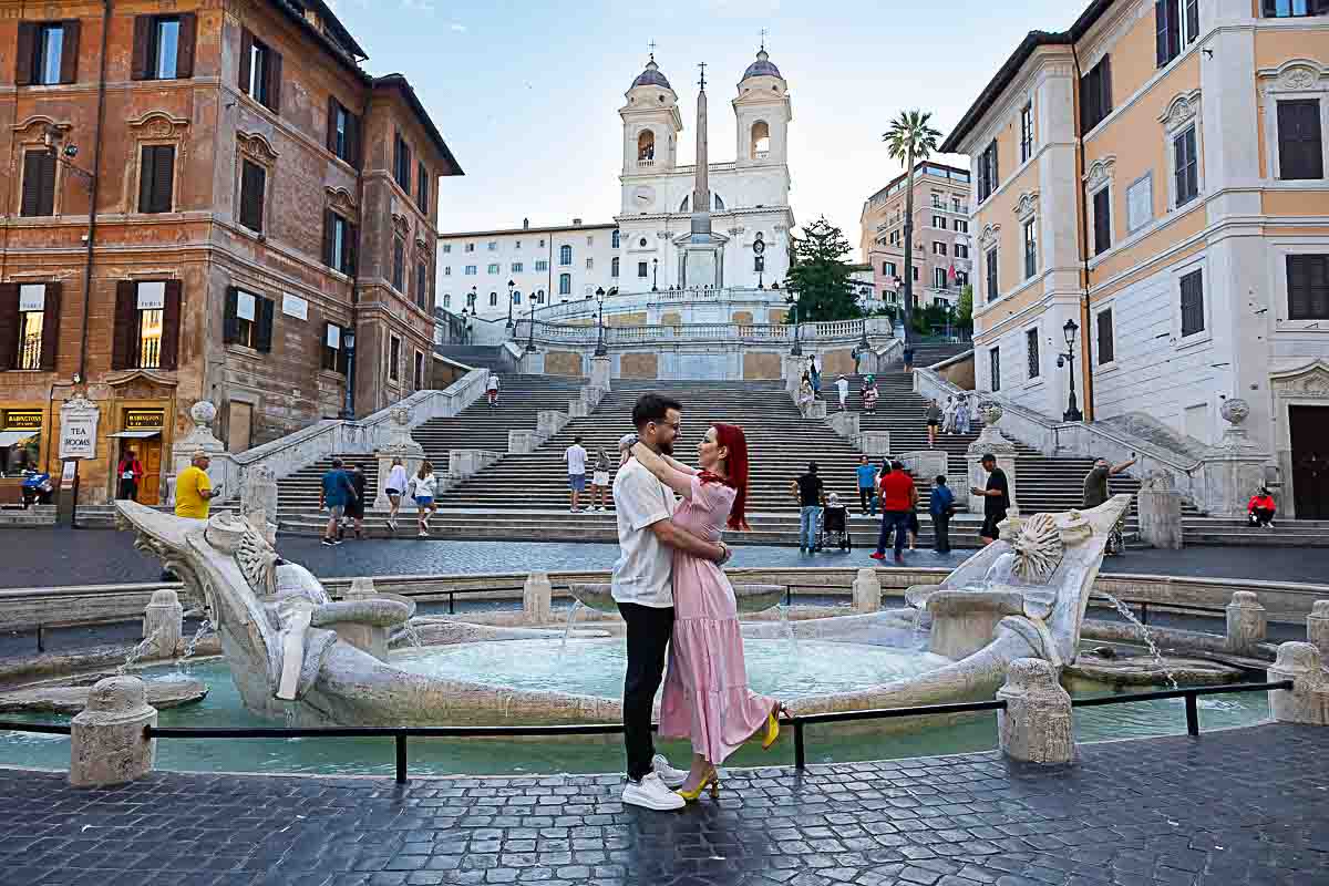 Couple posing beside the Barcaccia Fountain at sunrise during a romantic engagement photos
