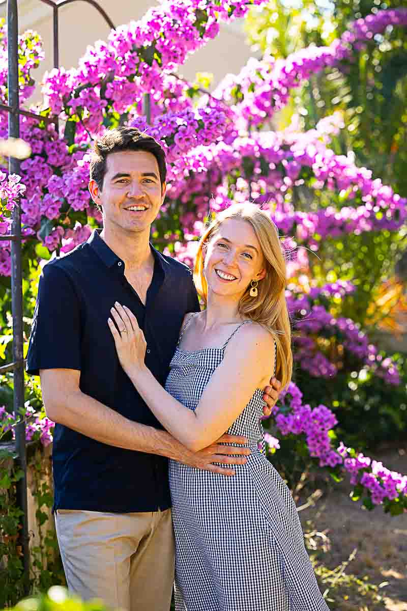 Posed before a bougainvillea fuchsia flower plant smiling and posing in front of the camera taking photos during a photoshoot in the park 