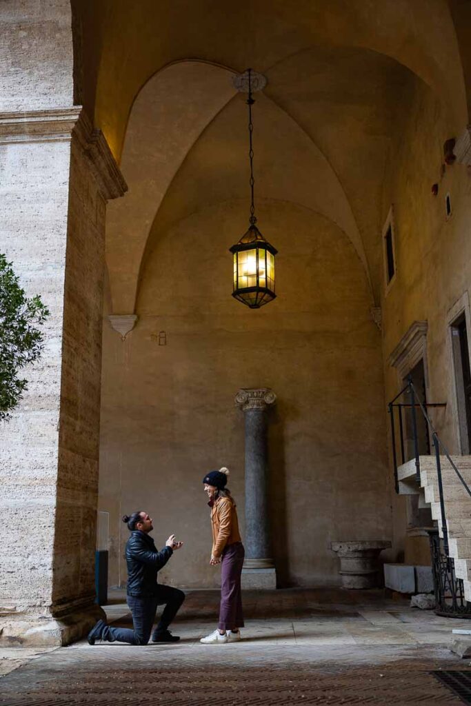Roman Proposal in Rome Italy knelling down to ask the big question underneath a portico with beautiful natural light shining through