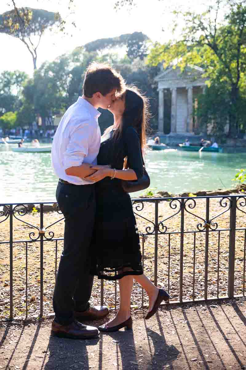 Couple kissing during a photoshoot in Rome's Borghese lake with a roman temple in the backdrop