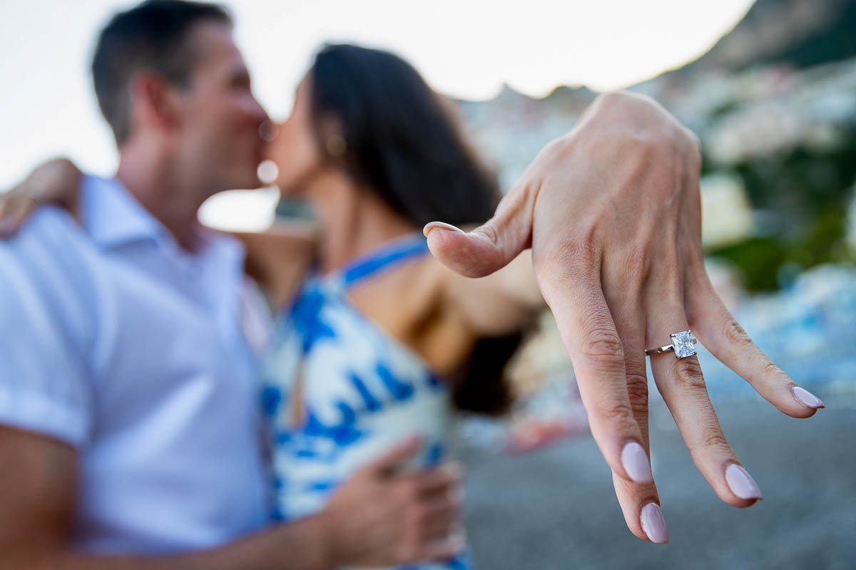 Showing the engagement ring while kissing blurred in the background engagement photo session