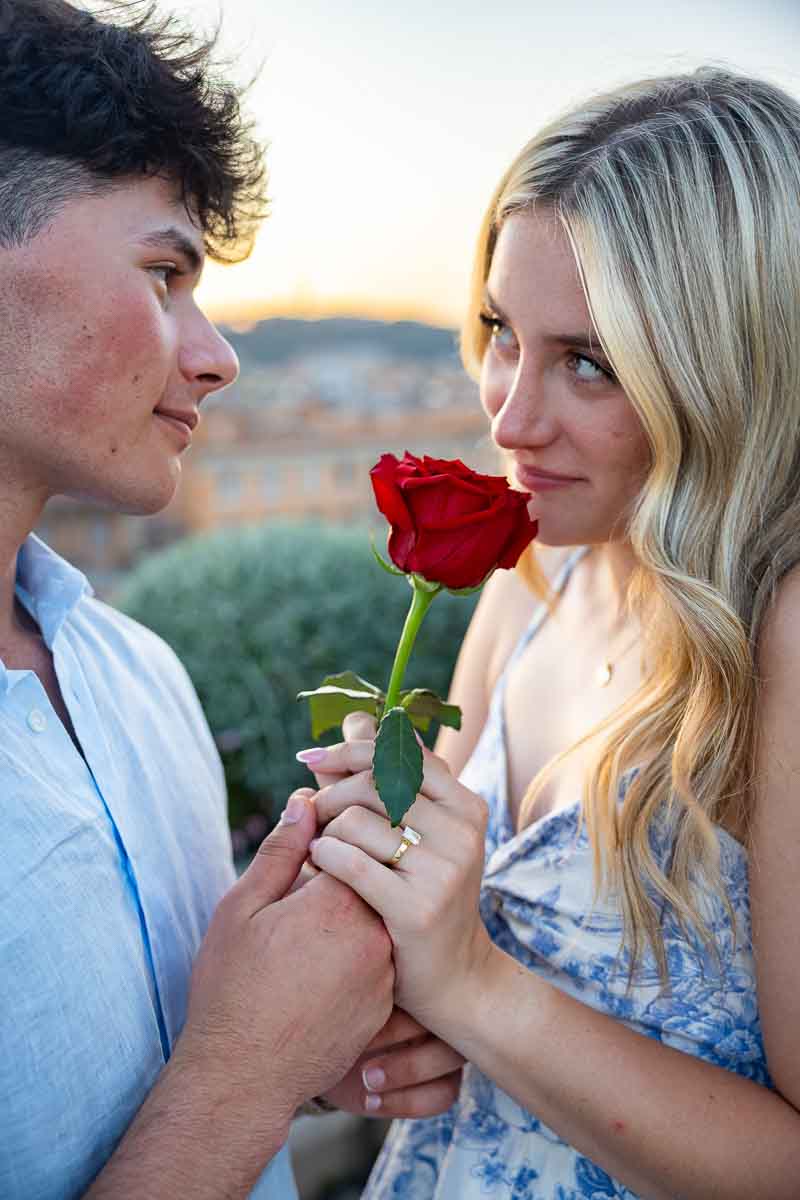 Nice image of a couple looking at each other while holding a rose and taking pictures during a photographer session
