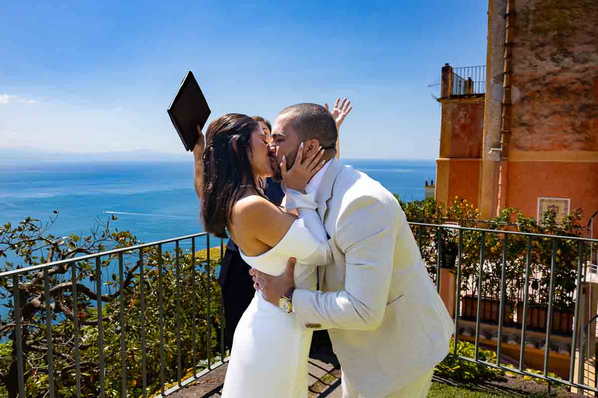 Just married picture of the newlyweds kissing with the celebrant celebrating as background