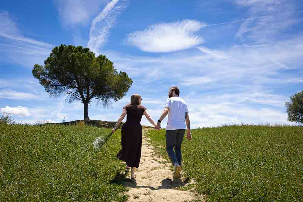 Walking up together holding hands while taking engagement photos together followed by a photographer capturing unique and creative couple pictures 