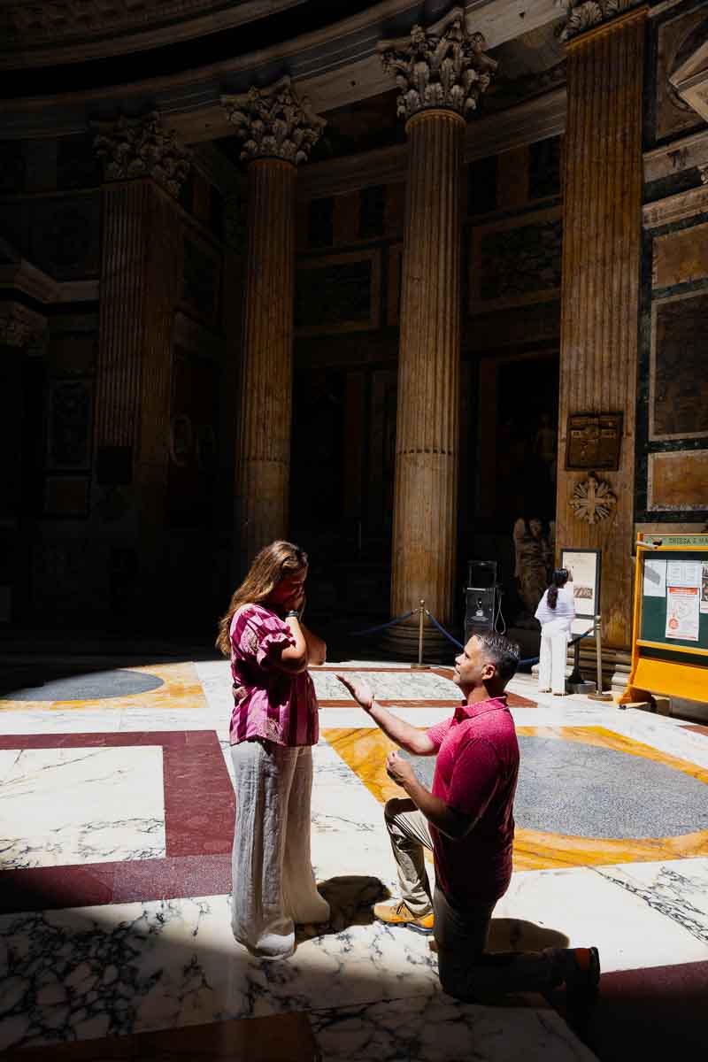Man kneeling during a marriage proposal beneath the oculus light inside the ancient Roman Pantheon during a surprise engagement photo shoot