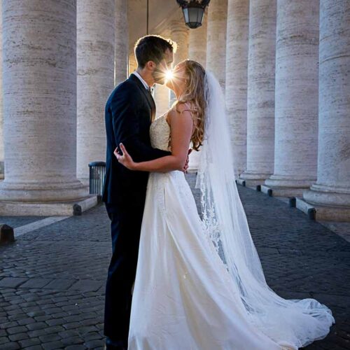 Sideways picture of bride & groom during a photographer session while kissing with the sun rays in between