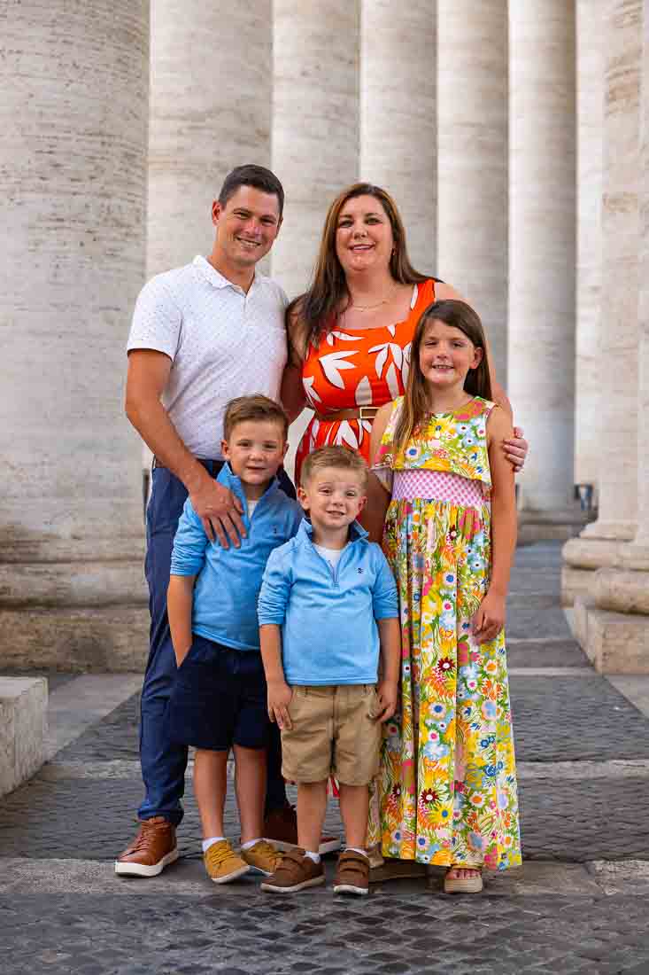Group portrait of multiple generations standing together beneath the colonnade at the Vatican in soft natural light during an outdoor portrait session