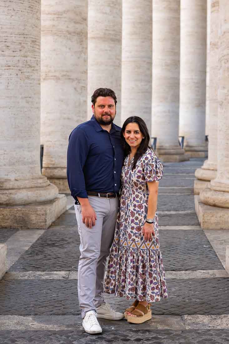 Couple standing together beneath the colonnade in Saint Peter’s Square during an outdoor portrait photo shoot in soft natural light with architectural symmetry in the background