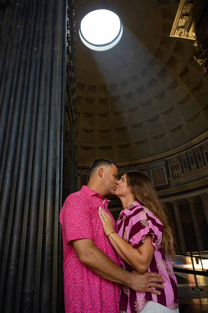 Couple kissing beside the monumental entrance doorway during an engagement photo shoot inside an ancient Roman landmark